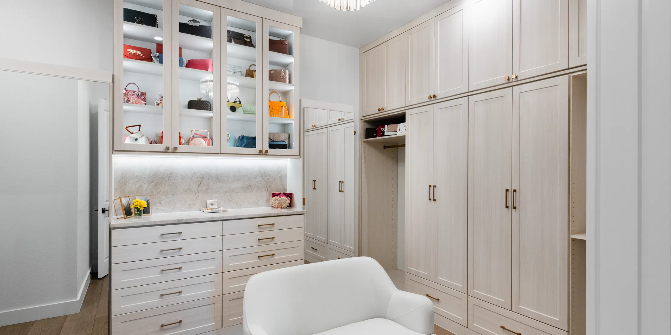 Boutique style walk-in closet with lit glass-front uppers and a full wall of wardrobes