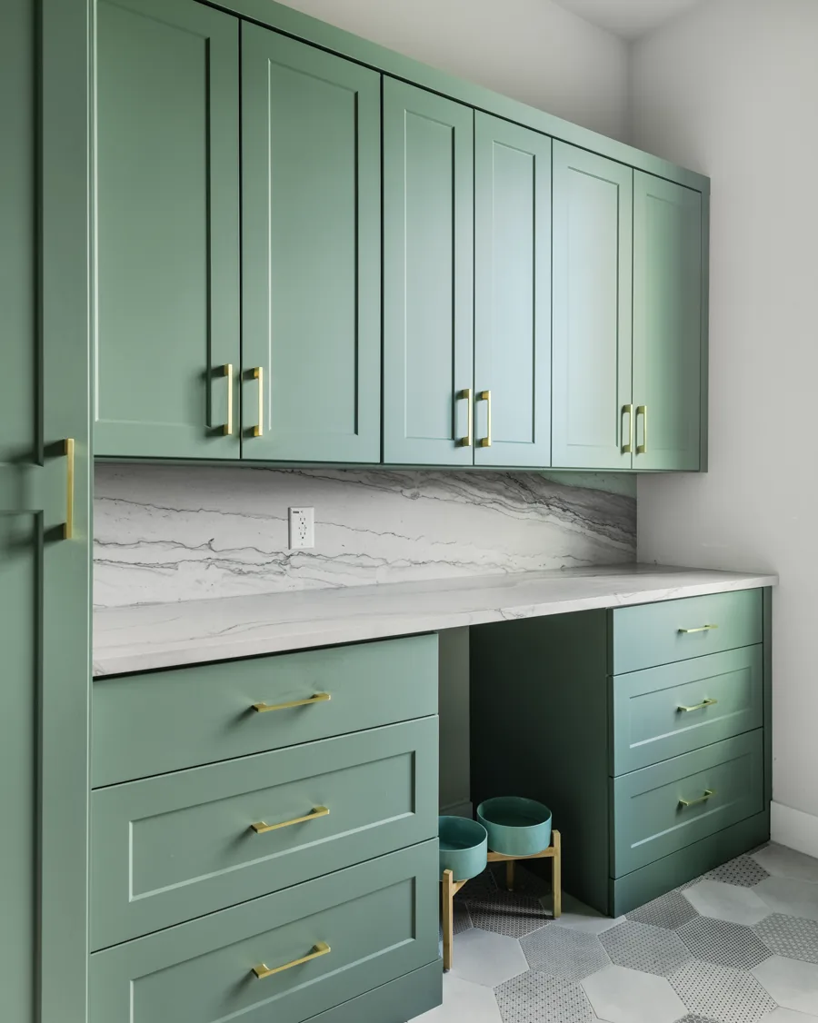 Green cabinetry with brass pulls, a marble backsplash and a built-in counter