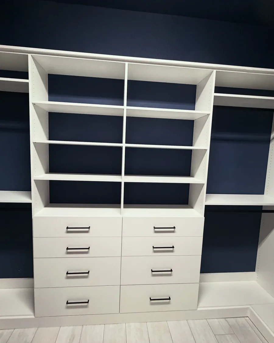 Custom closet with white shelving and drawer banks against navy back panels
