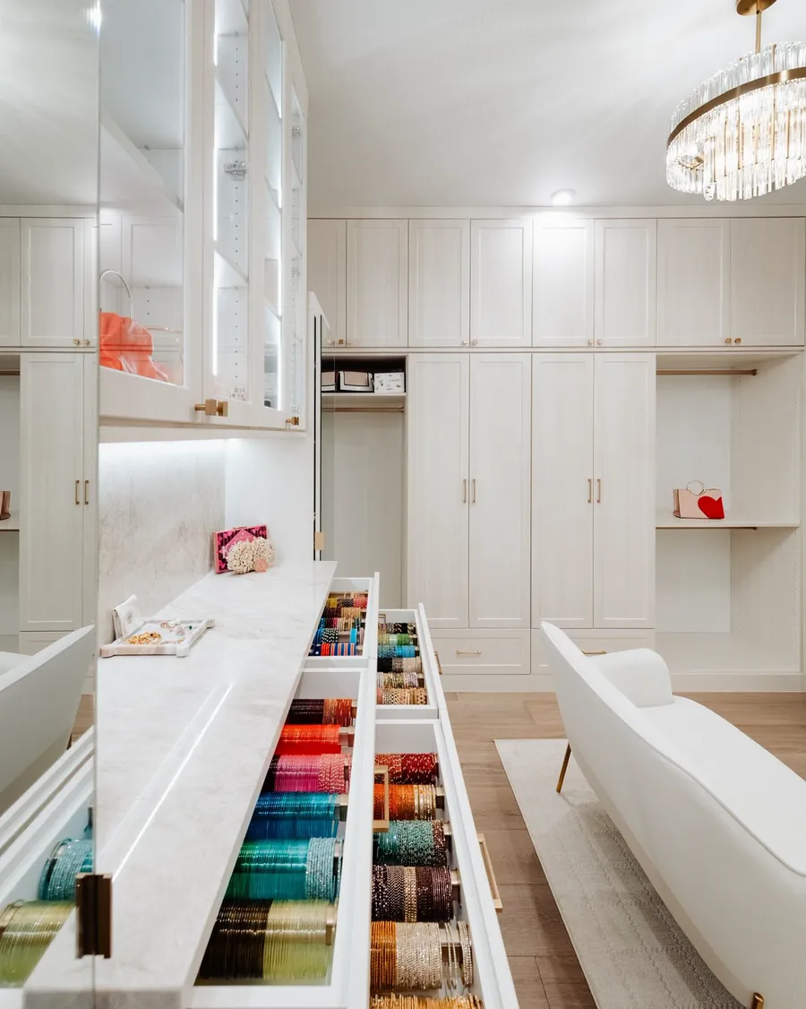 Custom closet with a long open drawer of folded clothing, a chandelier and a chaise