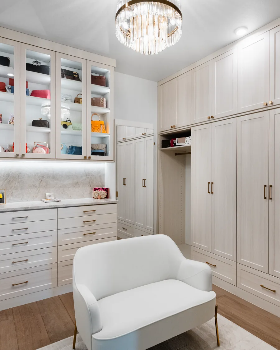 Custom walk-in closet with full-height wardrobes, glass-front uppers and a seat