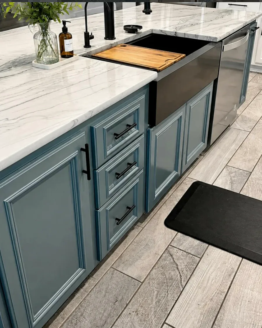 Blue kitchen cabinetry with marble counters, a farmhouse sink and black hardware