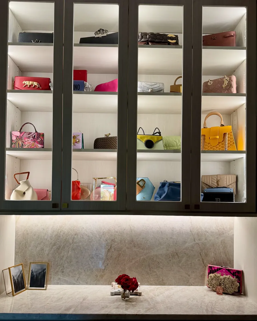 Lit glass-front closet cabinets displaying handbags above a quartzite counter