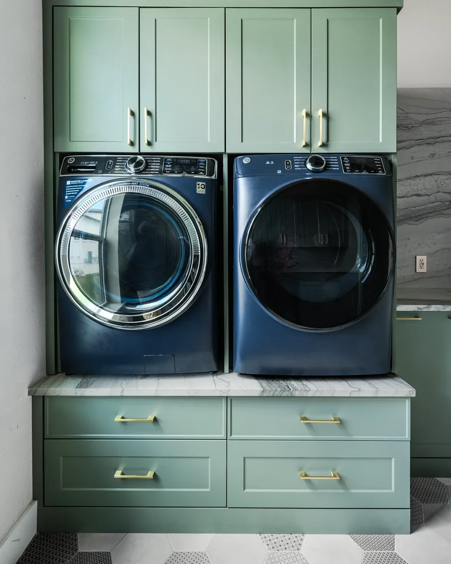 Green laundry room cabinetry with a marble counter over the washer and dryer