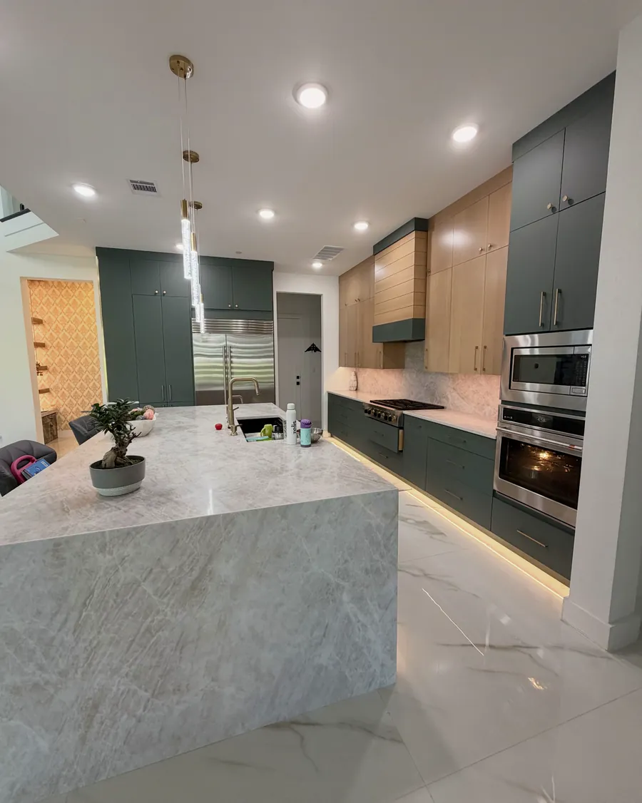 Kitchen island with a marble waterfall edge beside a dark green cabinet run