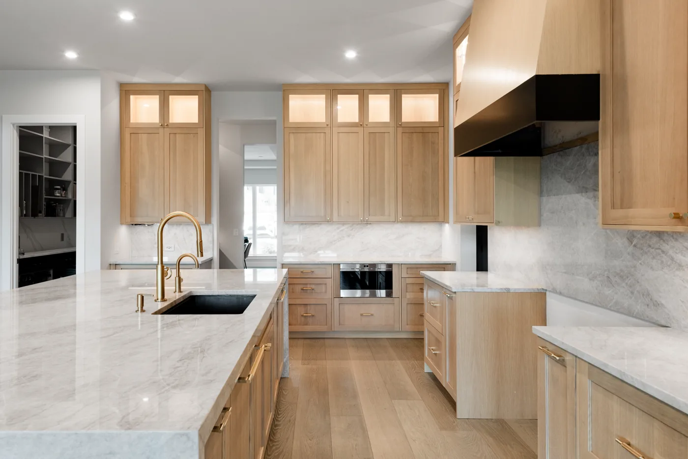 Kitchen with white oak cabinets, a marble island and a brass faucet