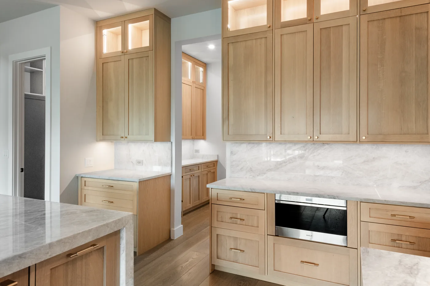 Kitchen with white oak uppers, marble counters and a built-in oven run