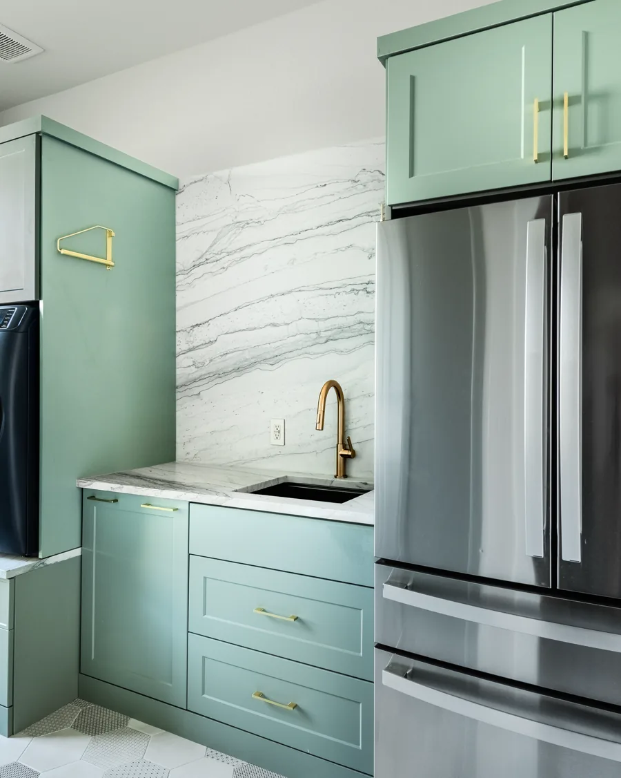 Laundry room with green cabinetry, a sink, front-load machines and a marble surround