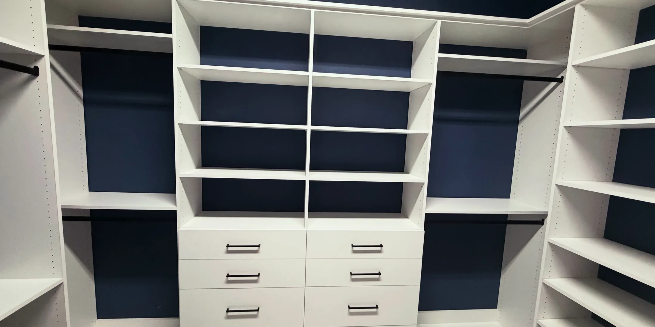 Walk-in closet with white shelving and drawer banks against navy back panels