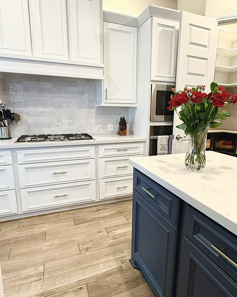 White kitchen cabinetry with a navy island, marble counter and gas cooktop