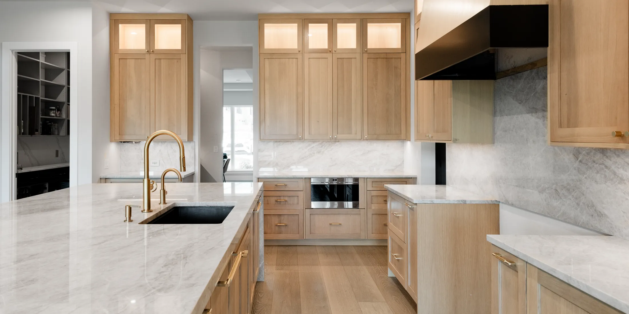Remodeled white oak kitchen with a marble island, brass tap and a black range hood