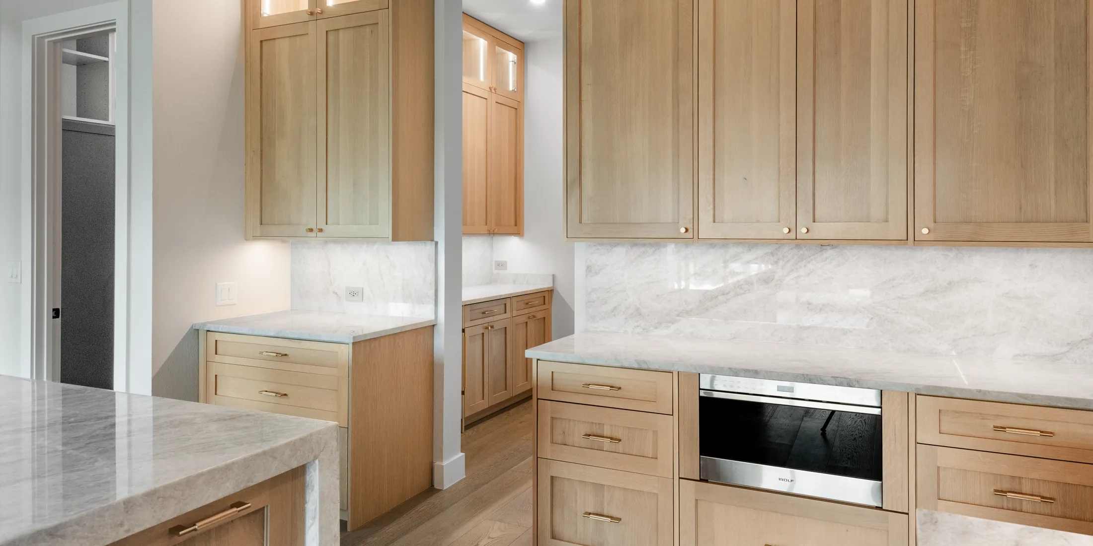 White oak pantry cabinetry with a marble backsplash and a built-in wall oven